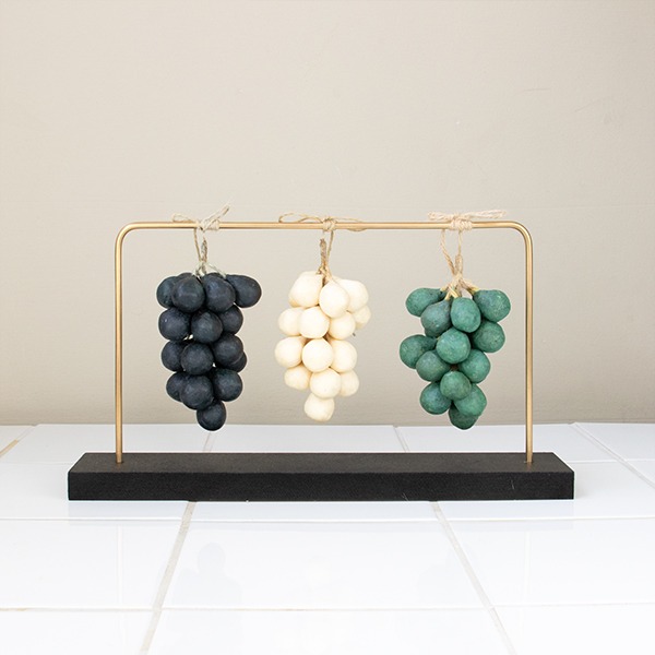 Grape shaped three soaps hanging from a metal tube that is supported with a black wooden block